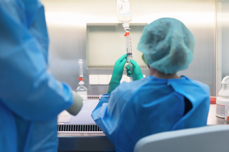 Medizinisches Fachpersonal in blauer Schutzkleidung, das eine Spritze in einem Labor vorbereitet. In der Germania Apotheke in Erfurt