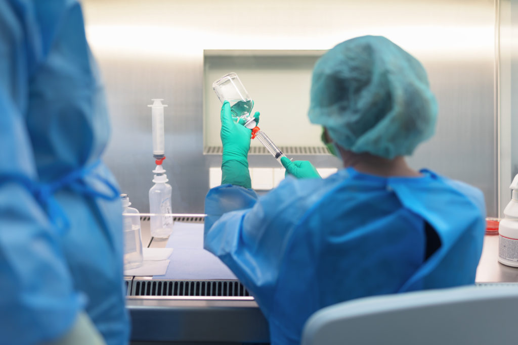 Laboratoriumsmitarbeiter in Schutzkleidung, der eine Glasflasche in der Hand hält und mit einer Spritze arbeitet. In der Germania Apotheke in Erfurt