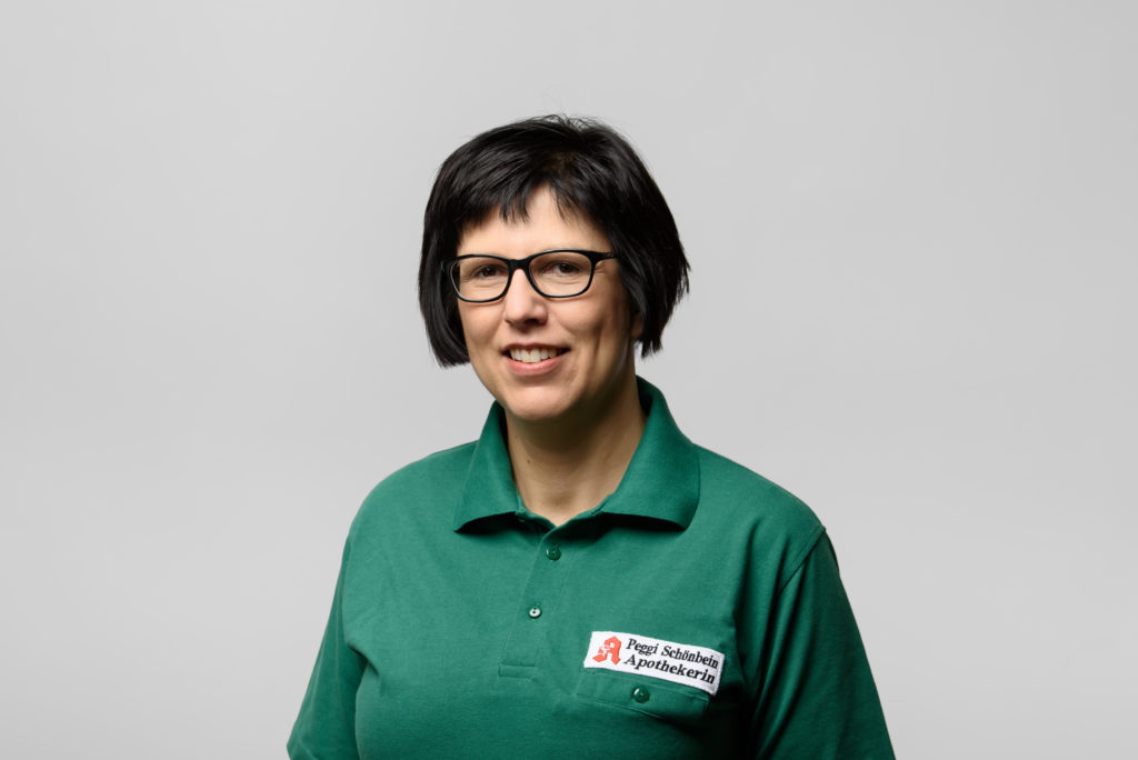 Frau Marquardt in grüner Uniform mit Brille lächelt in die Kamera. In der Germania Apotheke in Erfurt