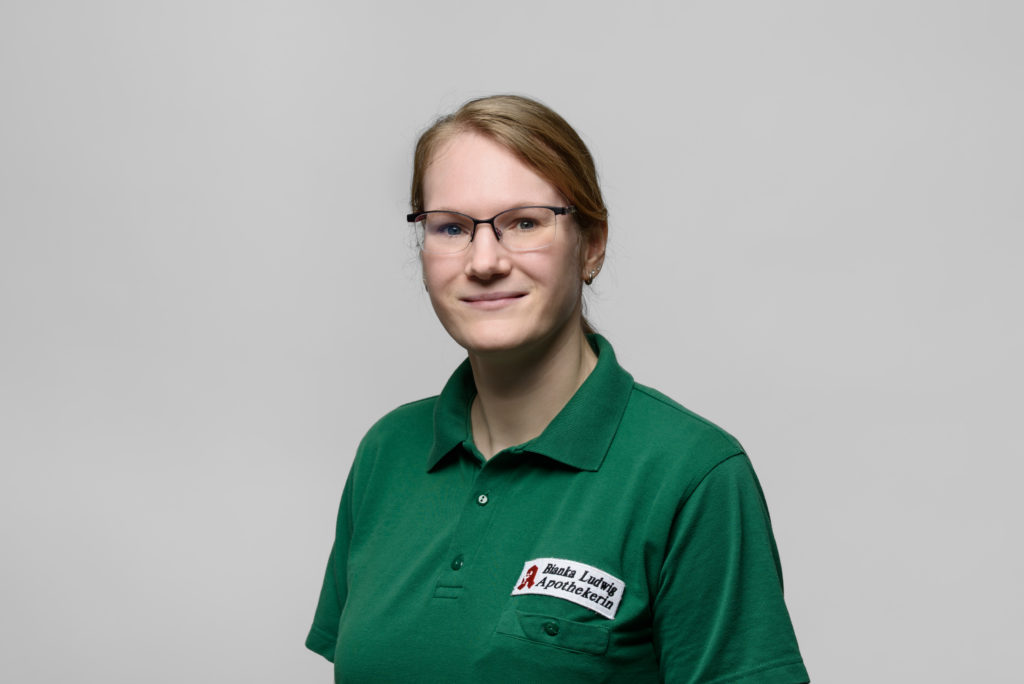 Frau Ludwig​ mit Brille in einem grünen Poloshirt mit dem Logo der Germania Apotheke Erfurt. In der Germania Apotheke in Erfurt