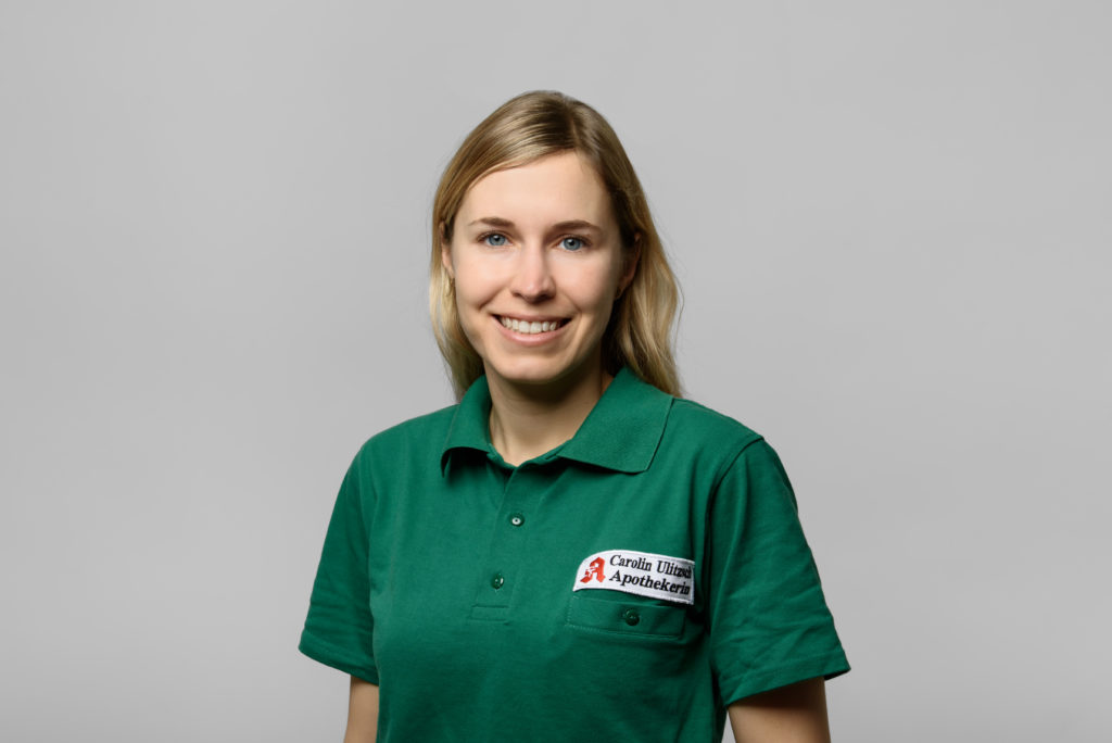 Frau mit langen blonden Haaren, die ein grünes Poloshirt mit einem Apothekenlogo trägt. In der Germania Apotheke in Erfurt