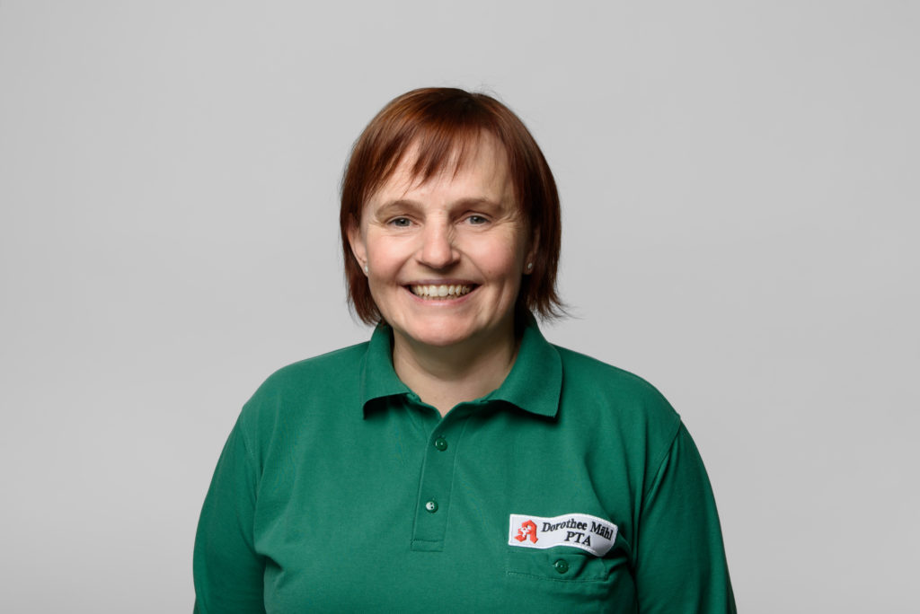 Lächelnde Frau Mähl mit kurzen braunen Haaren in einem grünen Polo-Shirt mit einem Abzeichen. In der Germania Apotheke in Erfurt