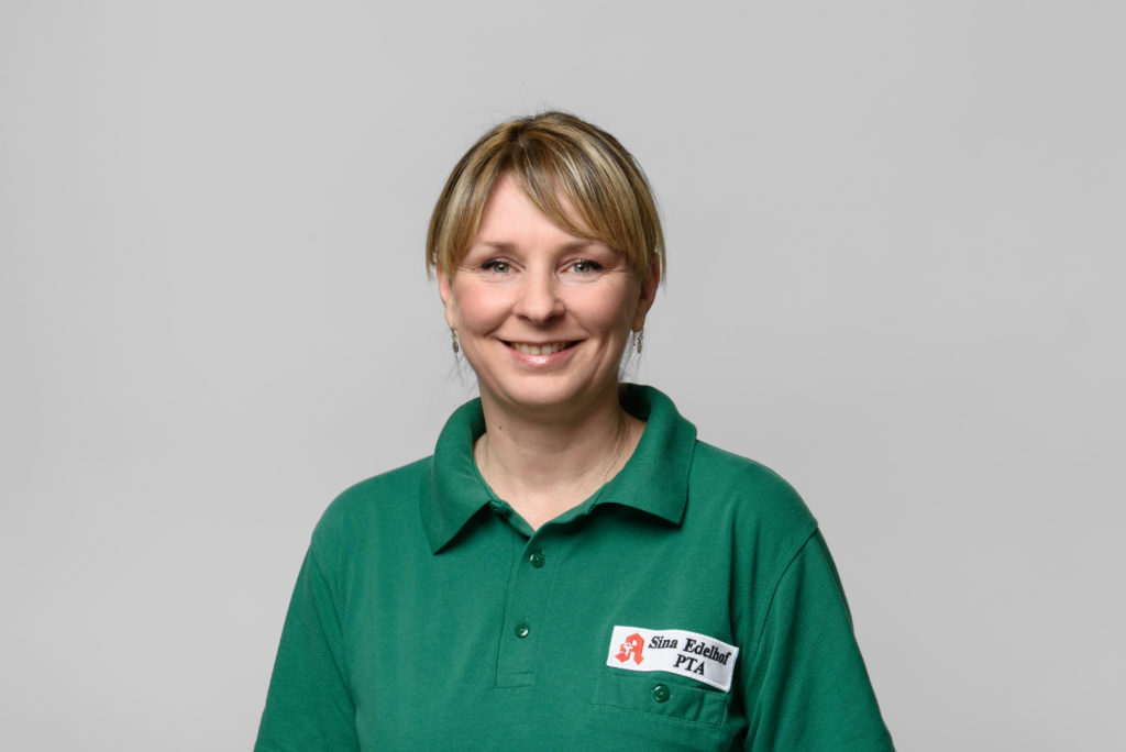 Frau Edelhof mit blonden Haaren in grüner Polo-Uniform, lächelnd und mit Namensschild. In der Germania Apotheke in Erfurt