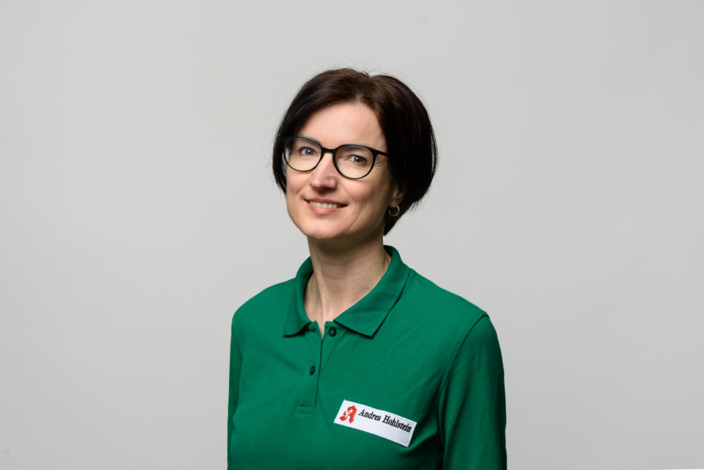 Frau Hohlstein mit Brille und grünem Poloshirt, lächelnd in die Kamera schauend. In der Germania Apotheke in Erfurt