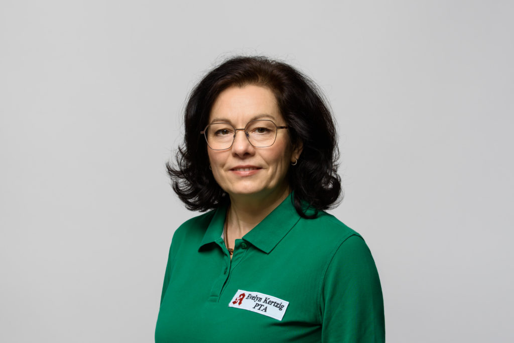 Frau Kertzig mit Brille trägt ein grünes Poloshirt mit PTA-Logo und schaut in die Kamera. In der Germania Apotheke in Erfurt